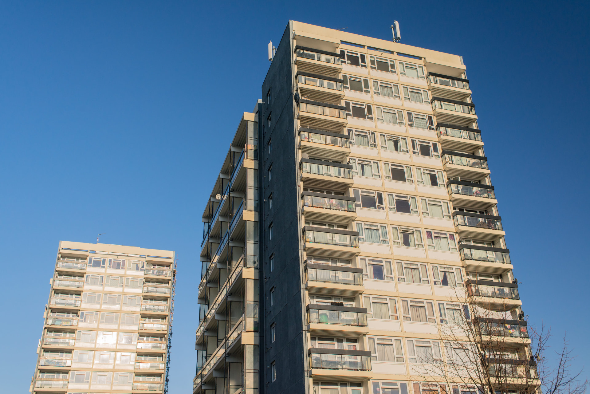 Tall UK residential blocks of flats with balconies against a clear blue sky